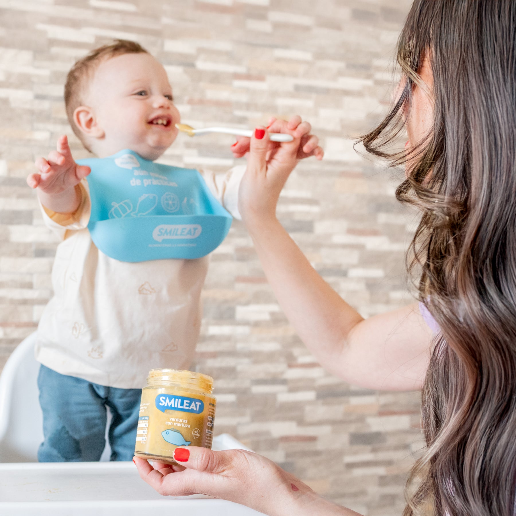 Mamá alimentando a un niño con tarrito ecológico de merluza y verduras