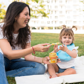 Mamá con niña en el parque comiendo un tarrito ecológico