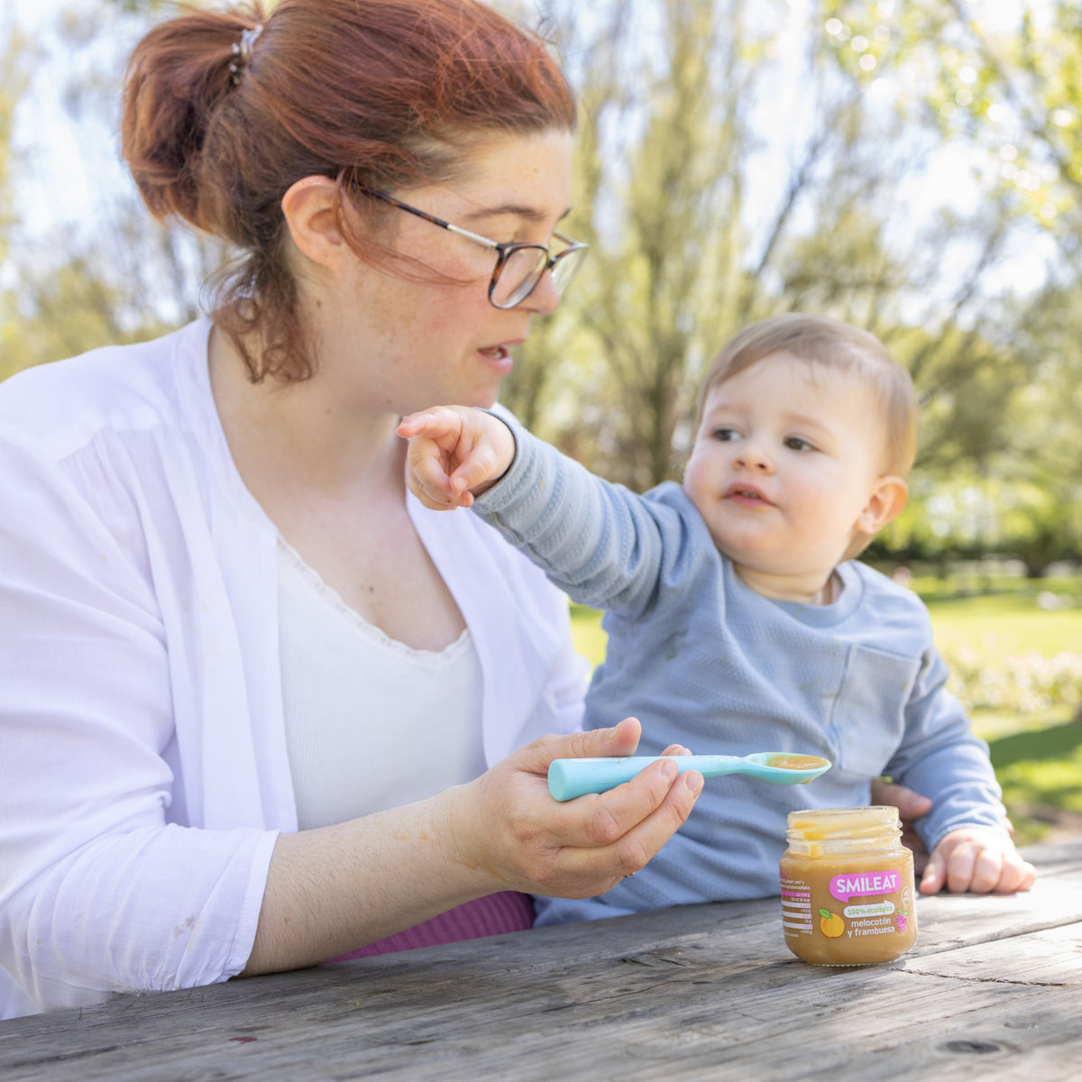 Mother feeding infant with organic peach and raspberry jars