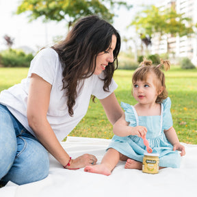Niña en el parque con mamá comiendo tarrito de comida